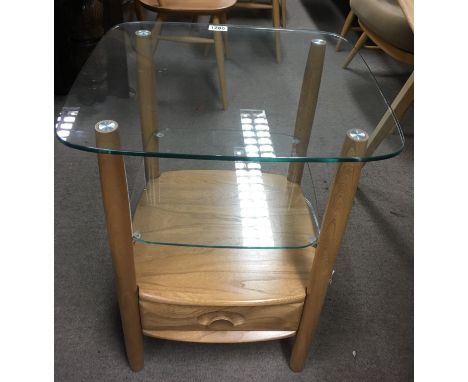 An Ercol light wood two tier glass top occasional table with single drawer.Approximately 65cm high, top 43.5x47.5 cm