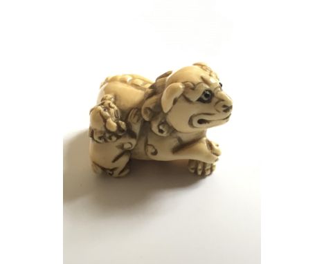 A Japanese carved Ivory Netsuke of the Meiji period, in the form of a temple dog with attached puppy, with applied eFixed, si