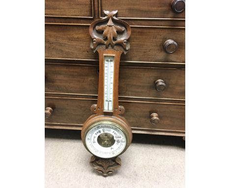 A vintage aneroid barometer and thermometer in carved oak case