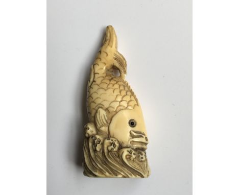 A Japanese Ivory Netsuke of the Meiji period 19th Century, carved in the form of a stylised fish with inset eFixed, above wav