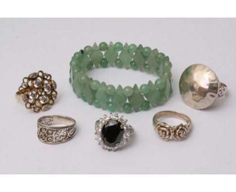 A jade bracelet comprised of spherical beads and diamond shaped pieces of jade alongside a collection of five rings, some sil