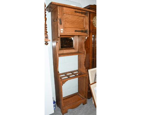 An Arts &amp; Crafts light oak hall stand with top cupboard section having copper strap hinges, a central mirror and raised o