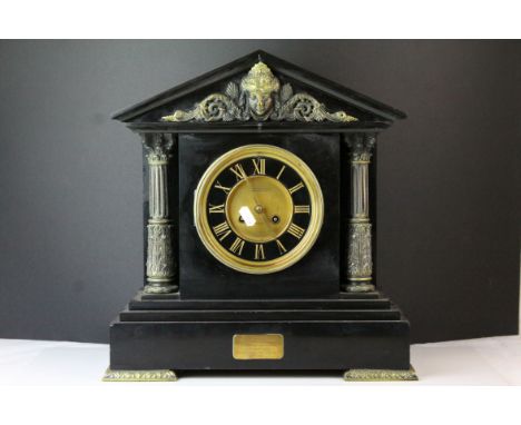A large slate mantle clock with brass Corinthian columns and mask decorated pediment. 