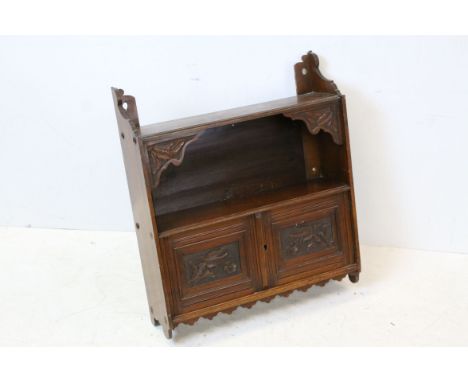 Late Victorian Arts and Crafts Mahogany Hanging Shelf with shaped supports, the two cupboard doors with floral carving, 58cms