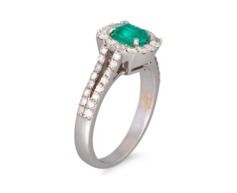 AN EMERALD AND DIAMOND CLUSTER RING, surrounded by round brilliant cut diamonds over a split diamond shank in 18ct white gold