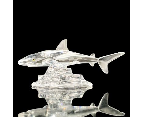 A clear crystal figure of a shark with melon-colored eyes that is swimming over some rocks. Swarovski backstamp. This item ha