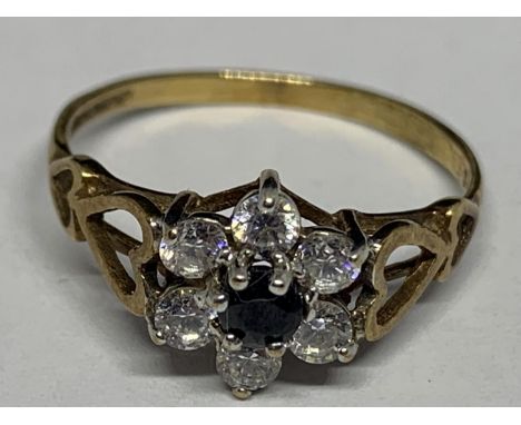 A 9 CARAT GOLD RING WITH A CENTRE SAPPHIRE AND CLEAR STONES IN A FLOWER DESIGN, HEARTS ON THE SHOULDERS SIZE M/N WITH A PRESE