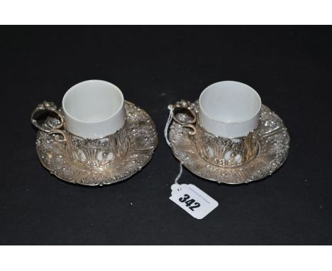 A pair of Continental 800 standard coffee cups on saucers with ceramic liners, decorated with putti, flowers and scrolls.