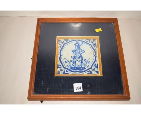 An 18th Century Delft tile depicting a soldier holding a gun, mounted in a frame.