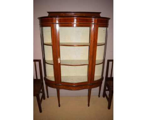 An Edwardian inlaid mahogany display cabinet with shaped front, the central glazed panel door enclosing cloth-lined shelves, 