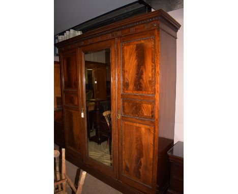 An Edwardian inlaid mahogany three door wardrobe, centre mirror panel door and two panel doors enclosing a fitted interior an