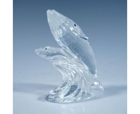 A clear faceted sculpture depicting a mother whale and her calf, both with blue eyes, riding the top of a wave. 1992 Swarovsk