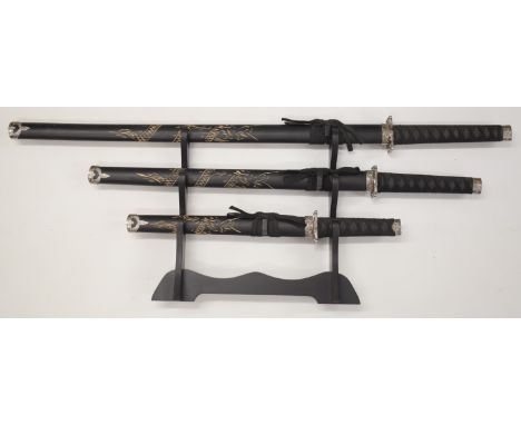 A set of three Japanese Samurai swords, all with bound handles and carved scabbards, largest 101cm long, on wooden display st