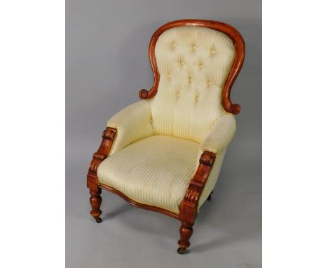 A Victorian stained oak spoon back armchair, with yellow striped patterned button back and serpentine over stuffed seat, rais