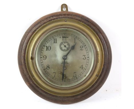 Brass bulkhead clock retailed by Barkers of Kensington, on oak back board, 28cm dia