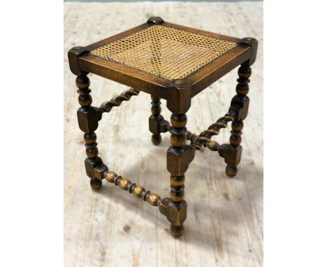 A 1920s oak cane seat stool on bobbin turned and block supports (h.48cm x l.35cm x w.35cm)