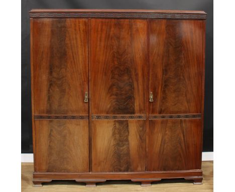 An early 20th century mahogany wardrobe, blind fretwork cornice above three doors, fitted with linen slides, drawers, a shelf