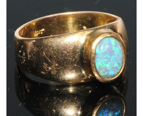 An 18ct gold and opal ring, the central oval cabochon stone with play of colour in blue and green, colette set, stamped 18ct,