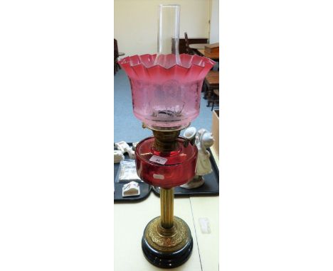 An oil lamp with cranberry glass reservoir, brass stem and pink shade