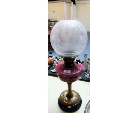 An oil lamp with brass support, opaque pink reservoir and etched shade