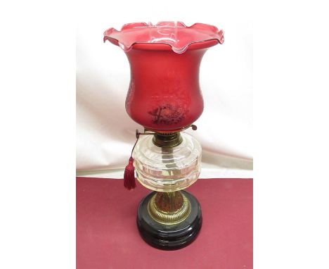 Early C20th oil lamp with cranberry etched shade, clear glass reservoir, on embossed brass base, terminating with circular eb