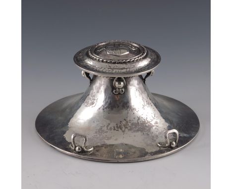 Alwyn Carr, an Arts and Crafts silver inkwell, London 1922, capstan form, planished, the lid cast with a coat of arms and mot