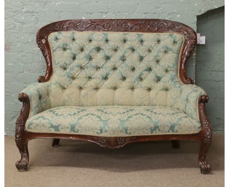 A carved mahogany sofa with green floral upholstery and deep button back.