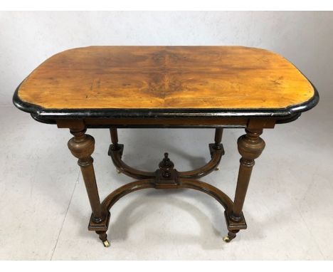 Ebonised and veneered occasional table with curved X-shaped stretcher on turned legs with castors, approx 107cm x 66cm x 77cm