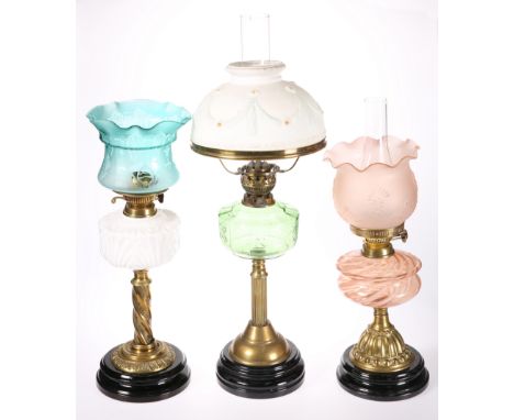 THREE VICTORIAN BRASS OIL LAMPS, the first with moulded opaque glass reservoir, the second with pink swirled glass reservoir,