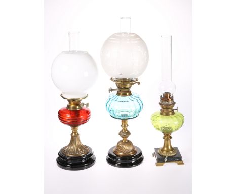 THREE VICTORIAN BRASS OIL LAMPS, the first with blue glass reservoir, the second with ruby glass reservoir, the third with gr