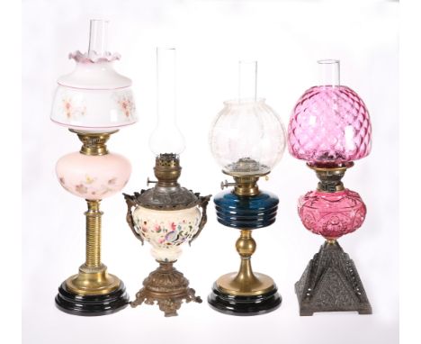 FOUR VICTORIAN OIL LAMPS, the first with cranberry glass reservoir and shade on a cast iron base, the second with blue moulde