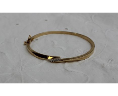 A yellow metal hinged bangle set with three brilliant cut diamonds, marked 14K, approximately 12 grams