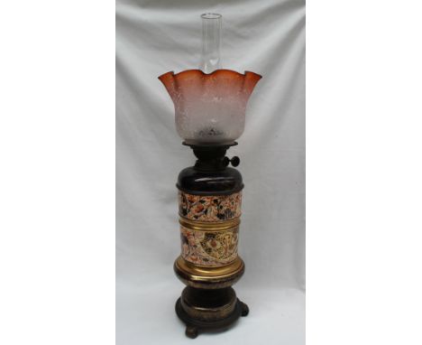 A Victorian pottery oil lamp, with a flared glass shade, the base in two sections decorated with flowers and leaves in redds 