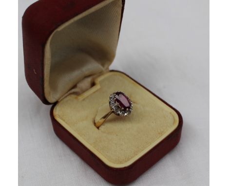 An 18ct gold ruby and diamond cluster ring, the oval shape ruby with brilliant cut diamond surround, to a white metal claw se