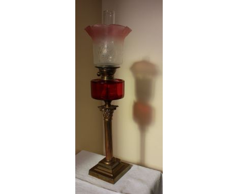 A Victorian cranberry glass oil lamp, the flared glass shade above a cranberry glass reservoir on a brass corinthian column, 