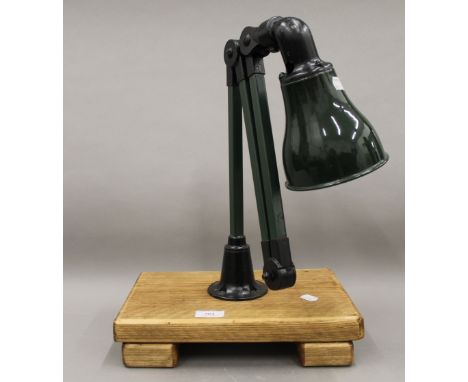 A green painted and enamel hinged machinists lamp mounted on a wooden stand. The stand 33 cm wide.