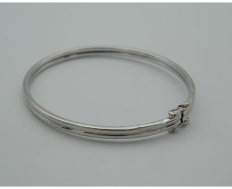 A 9 ct white gold bangle, housed in a velvet pouch. 6.5 cm wide (5.9 grammes)