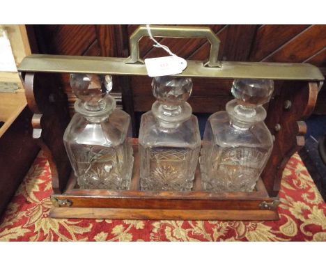 An early 20thC oak and brass three decanter Tantalus complete with decanters  Some minor chips to decanters, stoppers have ag