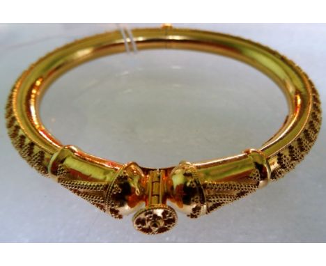 A yellow metal bangle of Middle Eastern origin, applied filigree wire and screw clasp to centre, stamped 22 carat. Condition 