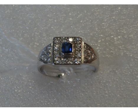 A white metal Art Deco-style ring, possibly 18 carat gold, set with central square cut sapphire, bordered by twelve diamonds,