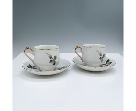 A charming set of two porcelain demitasse cups and saucers, each featuring a delicate hand-painted floral design with subtle 