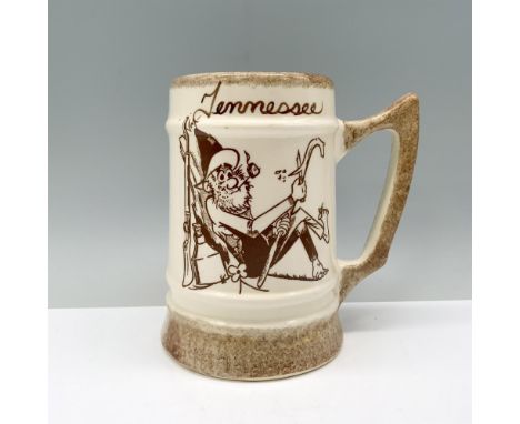A cream-colored mug embellished with stone-colored accents featuring artwork of a country man whittling a stick, with the wor