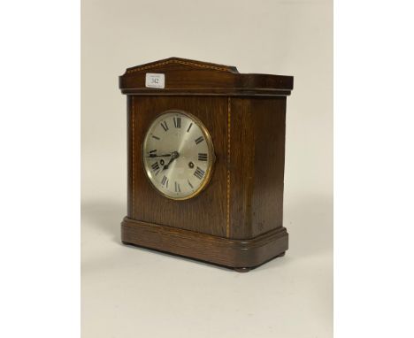 An early 20th century mantel clock in an inlaid oak case, the silvered dial with Roman chapter ring, eight day twin train mov