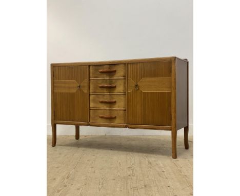 A mid century teak, mahogany, and walnut sideboard, fitted with four drawers flanked by a cupboard to each end, each enclosin