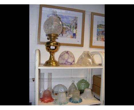 A brass oil lamp, in the company of assorted glass lamp shades - on two shelves  