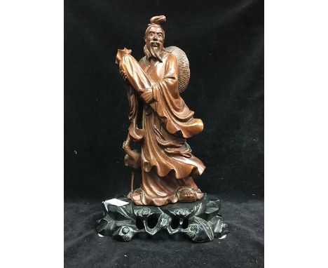 A Chinese carved wood figure of an immortal with scroll bag, his features picked out in bone, on a sperate hard wood carved b