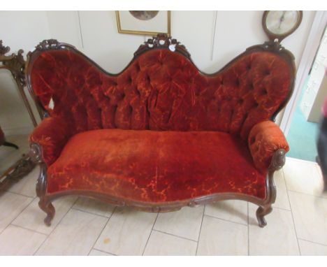 A Victorian walnut framed triple humpback Sofa with carved floral decoration and red plush upholstery, mounted upon scroll su