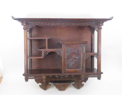 A Japanese hardwood Wall Cabinet with a pierced frieze above an arrangement of shelves and a cupboard door carved birds, 2ft 