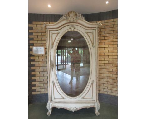 A 19th Century French cream and gilt painted Cabinet with oval glazed door, carved shell decoration and papered interior, on 