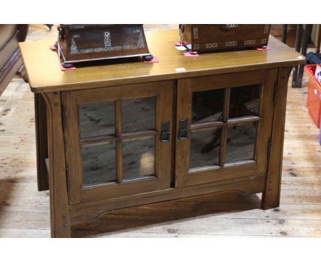 Sherry medium oak entertainment unit in Arts &amp; Crafts style having two glazed panel doors, 68cm by 101.5cm by 48cm.